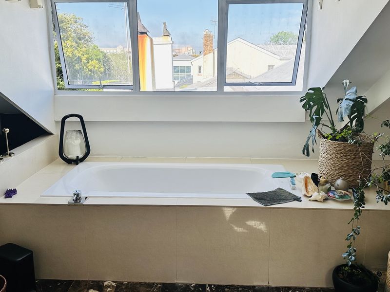 A bright bathroom featuring a built-in bathtub set against a large window with views, finished with neutral tiling.