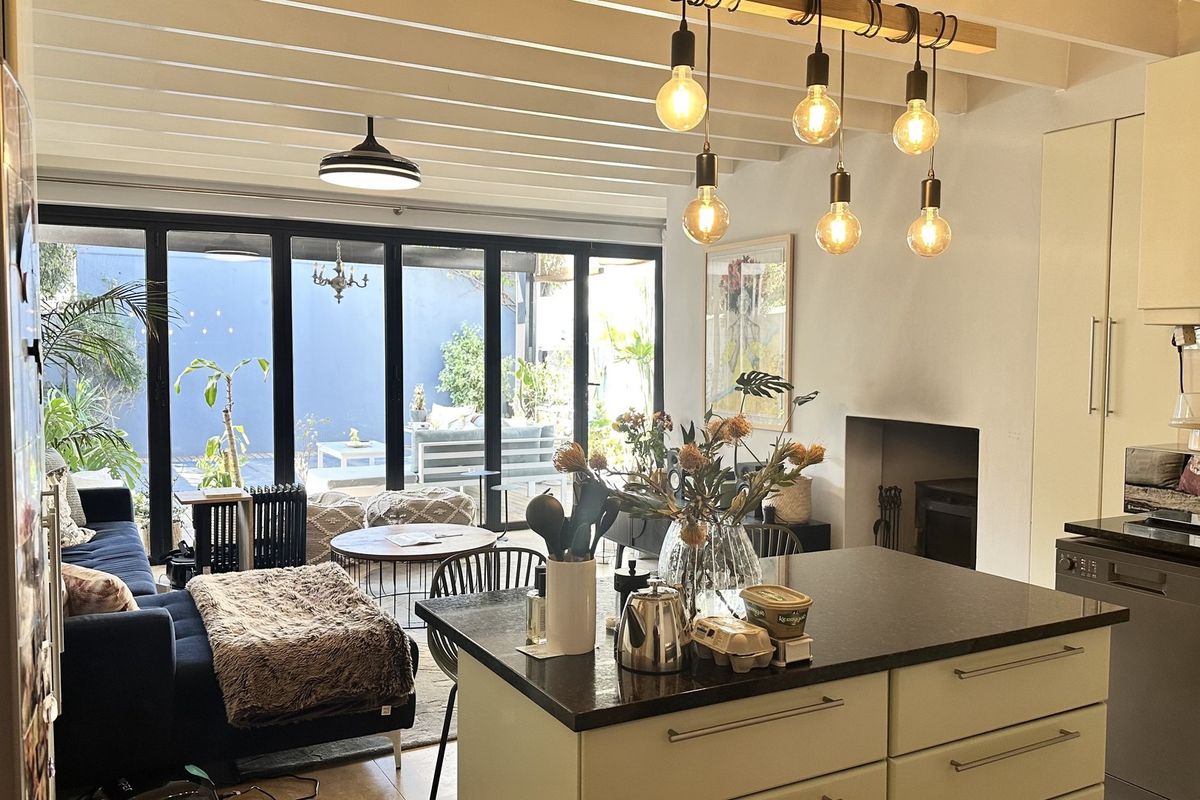 Open-plan living and kitchen area featuring a central island, exposed beam ceilings, fireplace, and large bi-fold doors opening to a rear patio.