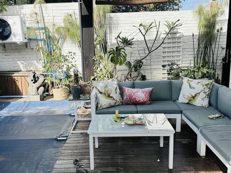 A covered outdoor patio area featuring timber decking and a painted brick wall, providing a functional space for outdoor relaxation.