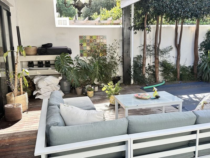 A covered outdoor patio area featuring timber decking, decorative wall tiling, and direct access to the interior through large sliding glass doors.