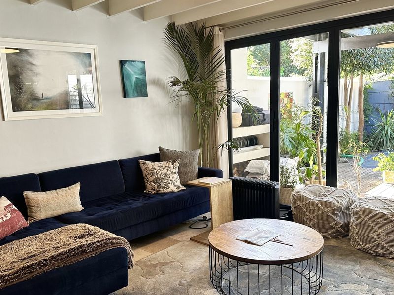 A bright living room featuring exposed ceiling beams and large black aluminium bifold doors that provide seamless access to the outdoor patio area.