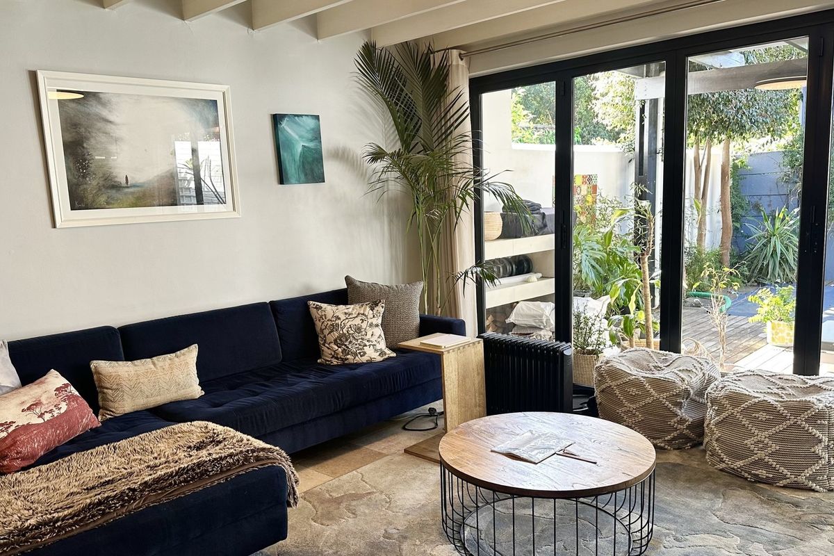 A bright living room featuring exposed ceiling beams and large black aluminium bifold doors that provide seamless access to the outdoor patio area.