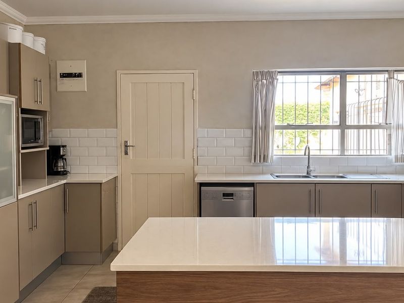 Modern kitchen featuring neutral cabinetry, stone countertops, a central island, subway tile backsplash, and integrated appliances.