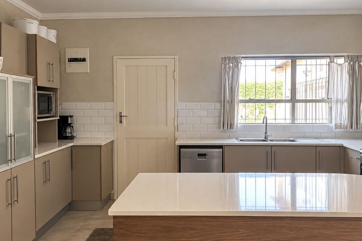 Modern kitchen featuring neutral cabinetry, stone countertops, a central island, subway tile backsplash, and integrated appliances.