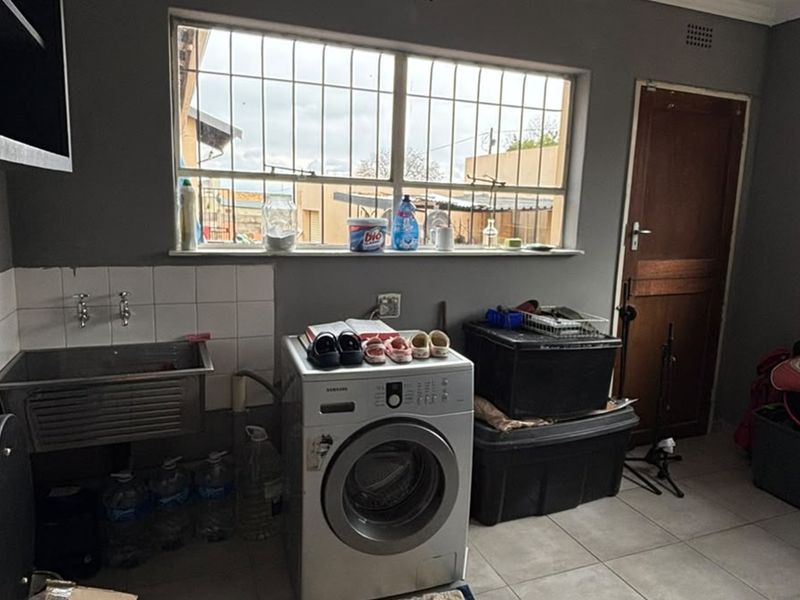 A functional laundry room featuring a stainless steel sink, tiled splashback, and tiled flooring, with security bars installed on the windows.
