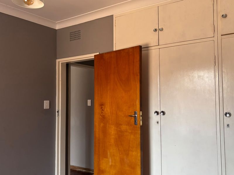A bedroom featuring built-in cupboards with overhead storage and a classic timber door, offering a neutral canvas for interior updates.