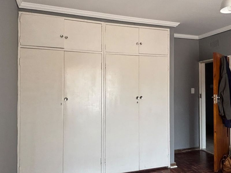 A bedroom featuring built-in cupboards with overhead storage, crown molding, and traditional parquet flooring.
