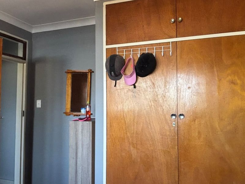 A bedroom featuring a built-in wooden wardrobe with overhead storage and grey painted walls.