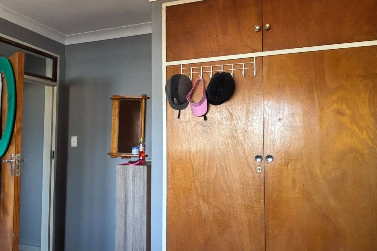 A bedroom featuring a built-in wooden wardrobe with overhead storage and grey painted walls.