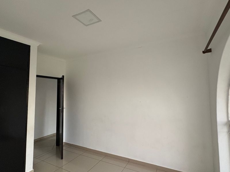 An empty bedroom featuring tiled flooring, a built-in wardrobe, and a distinctive arched window providing natural light.