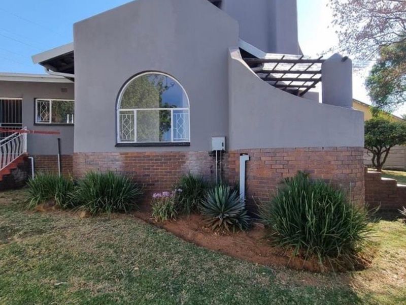 Rear view of the property featuring a grey rendered facade with a brick base, arched window, and an attached pergola structure.