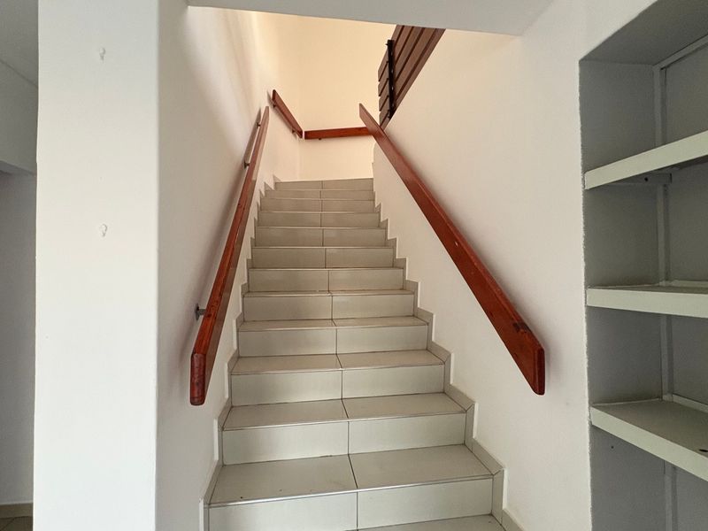 A bright staircase featuring tiled steps, wooden handrails, and integrated built-in shelving, providing a clean and functional transition between levels.