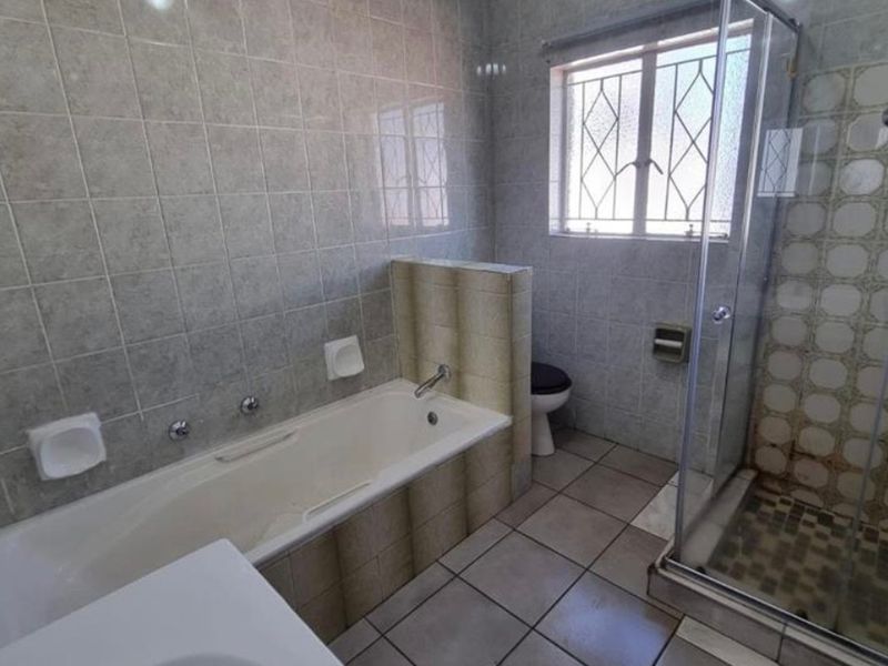 A functional bathroom featuring a built-in bathtub, a separate glass-enclosed shower, and tiled finishes throughout.