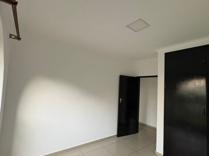 A bright, empty bedroom featuring tiled flooring, built-in cupboards, and a distinctive arched window, offering a clean and neutral space.