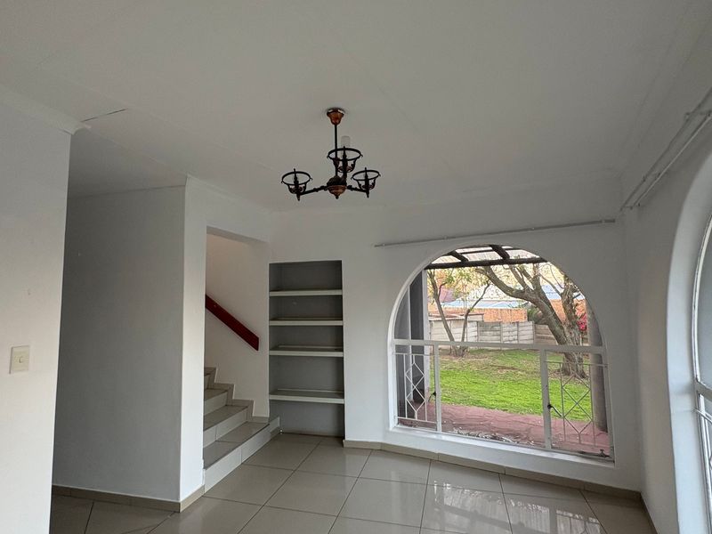 An empty living area featuring large arched windows, built-in shelving, tiled flooring, and direct access to a staircase.