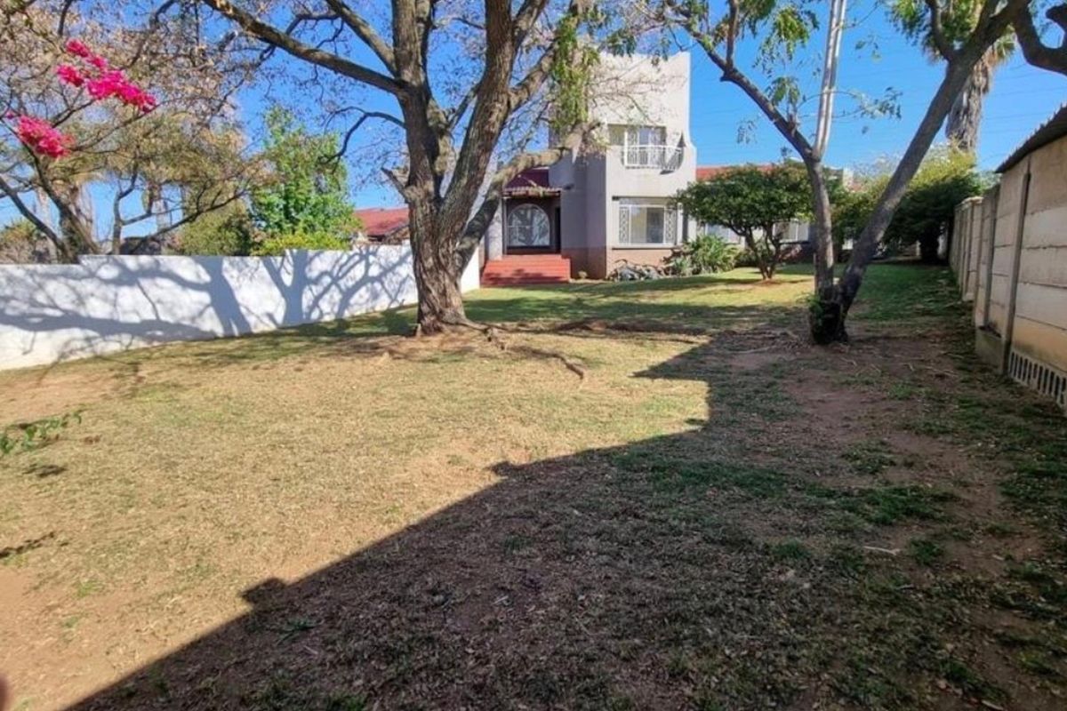 A spacious rear garden featuring mature trees, a lawn area, and a precast concrete boundary wall, providing a private outdoor space.