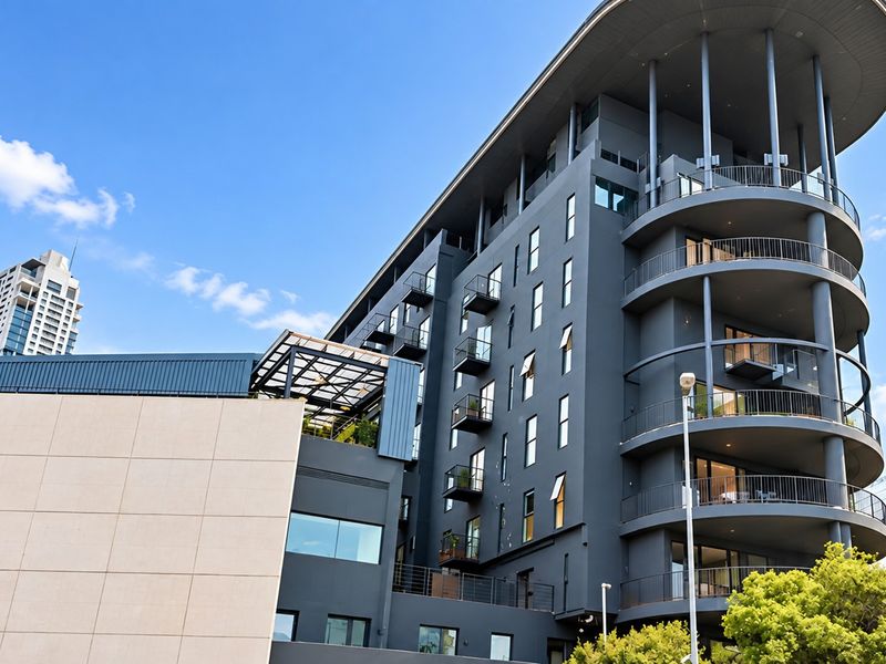 A modern multi-story apartment building featuring a dark grey facade, curved balconies with metal railings, and a contemporary architectural design.