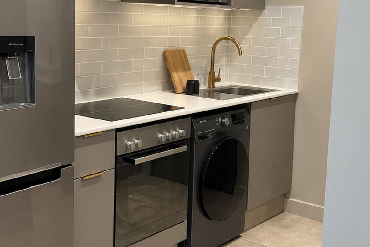Modern kitchen featuring grey cabinetry, quartz countertops, subway tile backsplash, brass faucet, and integrated appliances including an oven and hob.