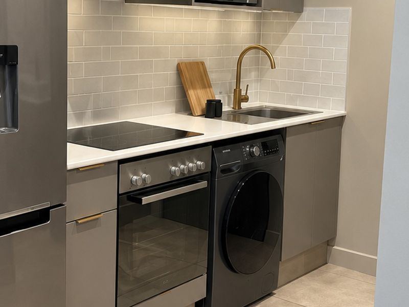 Modern kitchen featuring grey cabinetry, quartz countertops, subway tile backsplash, brass faucet, and integrated appliances including an oven and hob.