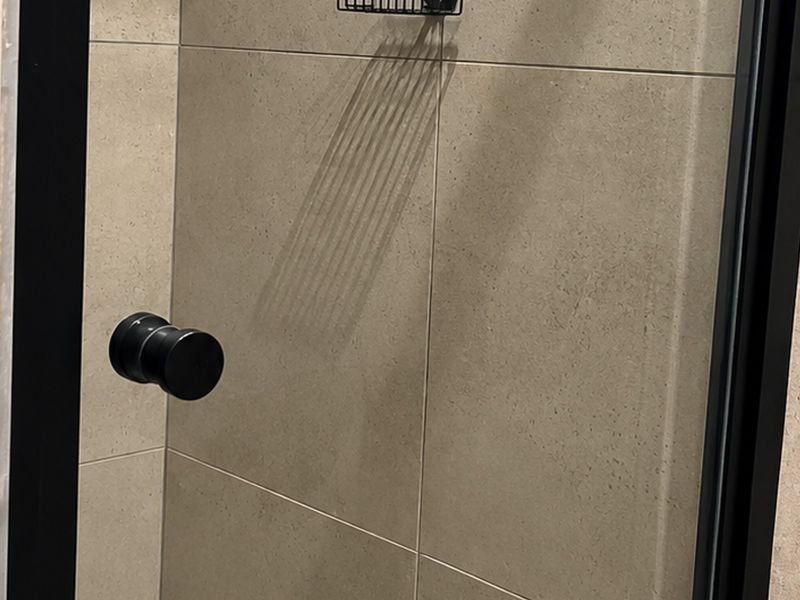 A modern shower enclosure featuring sleek black framing and neutral-toned ceramic wall tiles.