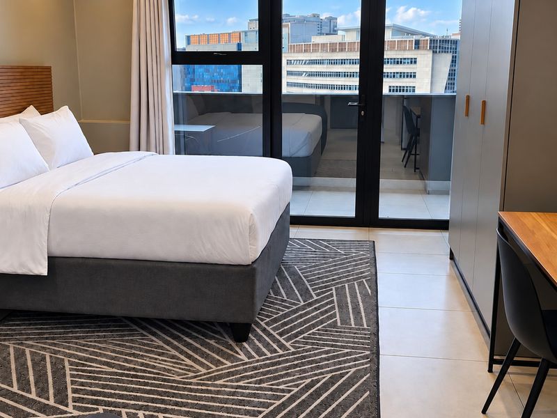 Modern bedroom featuring tiled floors, a built-in wardrobe, and large sliding glass doors providing access to a private balcony with city views.