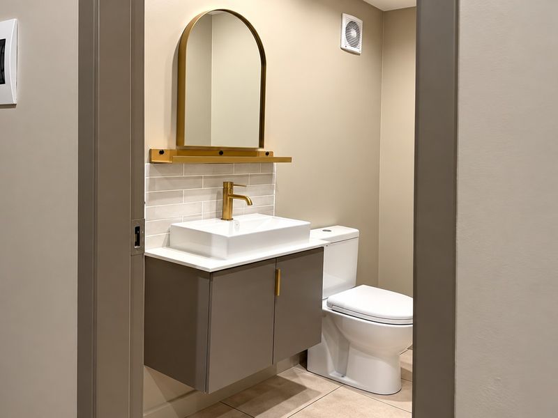 A modern, well-maintained bathroom featuring a wall-mounted vanity, brass fixtures, an arched mirror, and neutral subway tile backsplash.