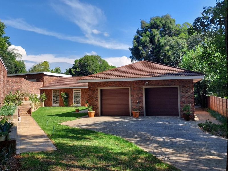 A well-maintained brick house featuring a double garage, paved driveway, and a neat front garden area.
