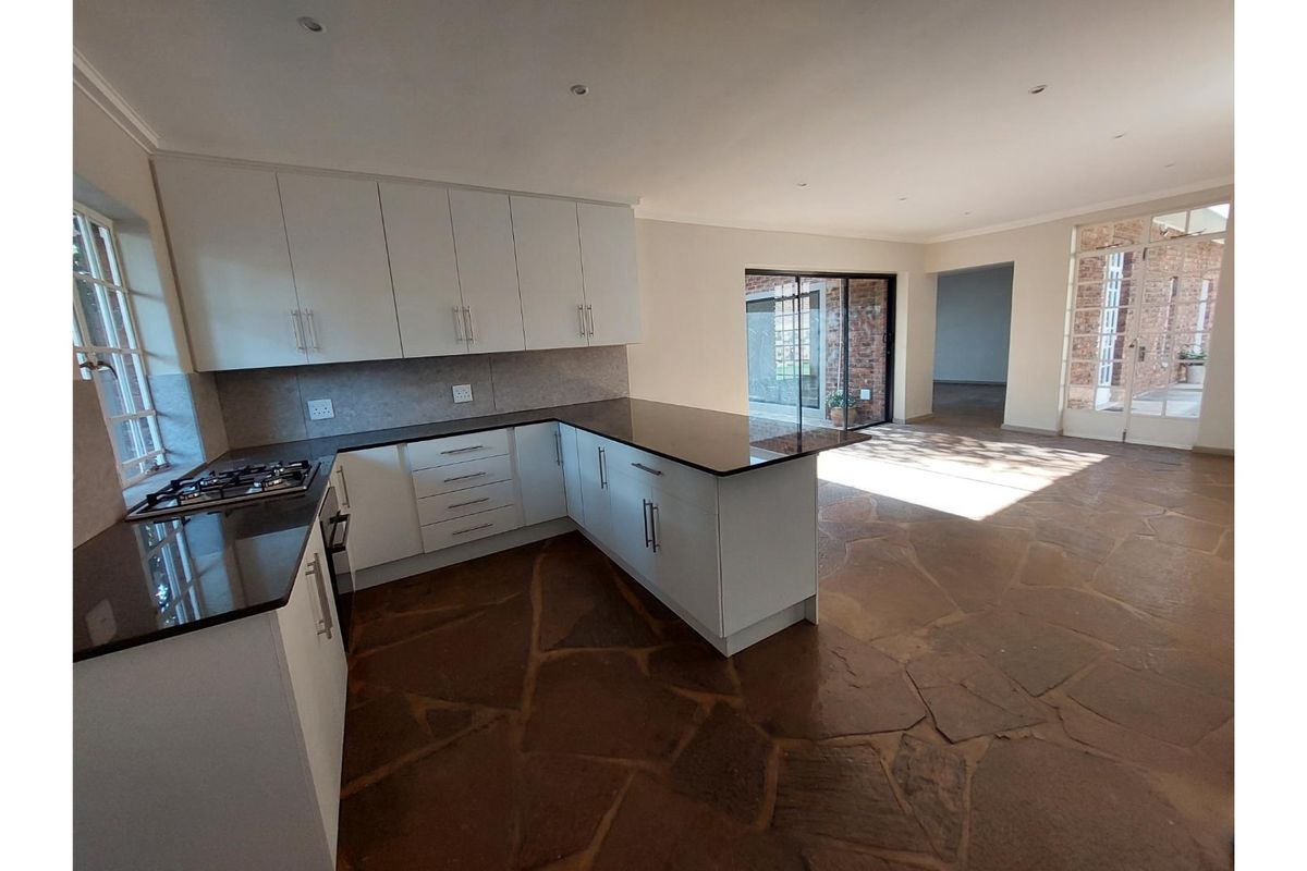 Spacious open-plan kitchen featuring white cabinetry, granite countertops, gas hob, and unique stone flagstone flooring, flowing into a bright living area with garden access.