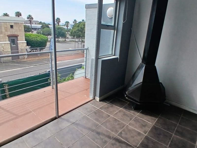 An empty living area featuring tiled flooring, a modern freestanding fireplace, and direct access to a private balcony through sliding glass doors.
