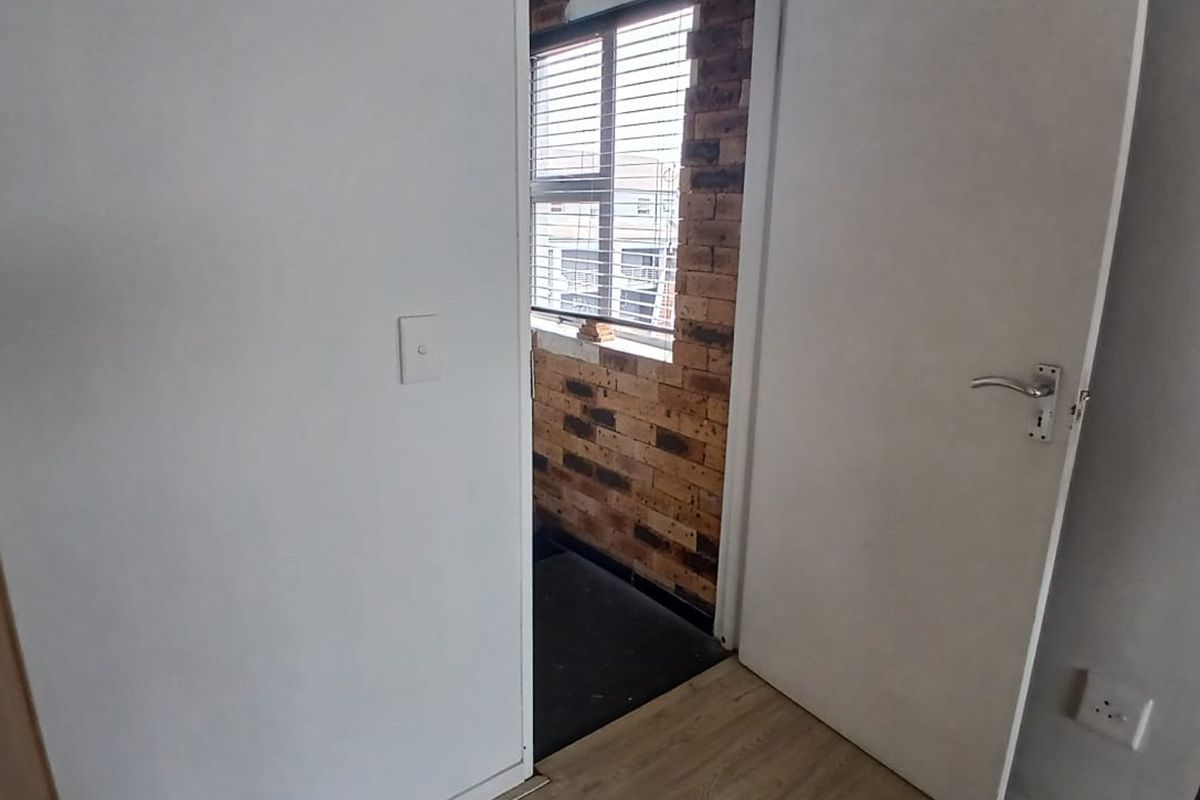 A view into a bedroom featuring laminate flooring and an exposed brick wall section near the window.