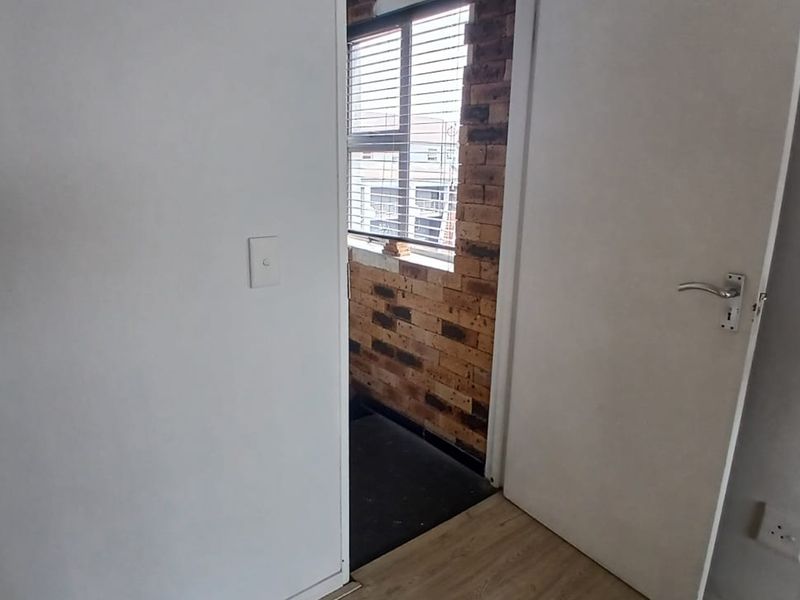 A view into a bedroom featuring laminate flooring and an exposed brick wall section near the window.