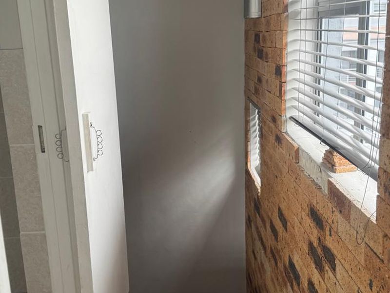 A narrow hallway featuring an exposed brick wall, venetian blinds, and visible ventilation infrastructure requiring finishing touches.