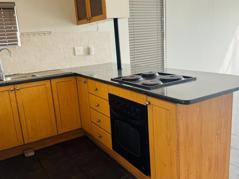 A functional kitchen featuring wooden cabinetry, granite countertops, a built-in oven with electric hob, and tiled backsplash.