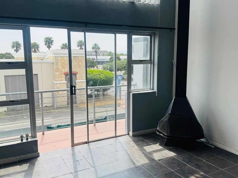 An empty living room featuring tiled flooring, a freestanding fireplace, and a sliding glass door leading to a balcony with street views.