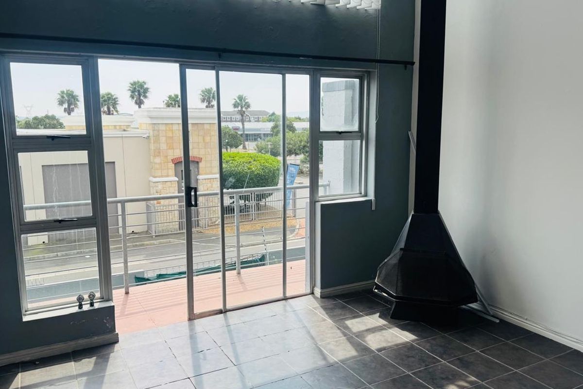 An empty living room featuring tiled flooring, a freestanding fireplace, and a sliding glass door leading to a balcony with street views.