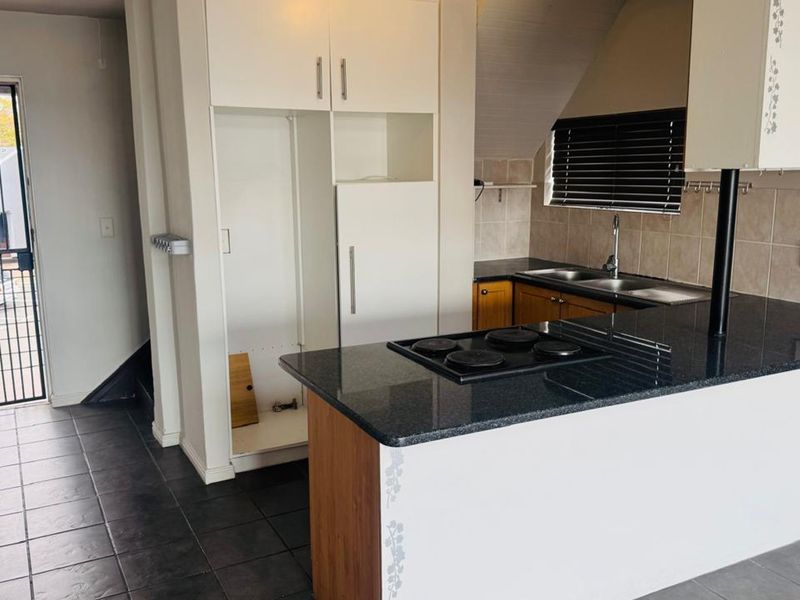 A functional kitchen featuring dark granite countertops, an electric hob, built-in cabinetry, and tiled flooring, with an adjacent security gate leading outdoors.