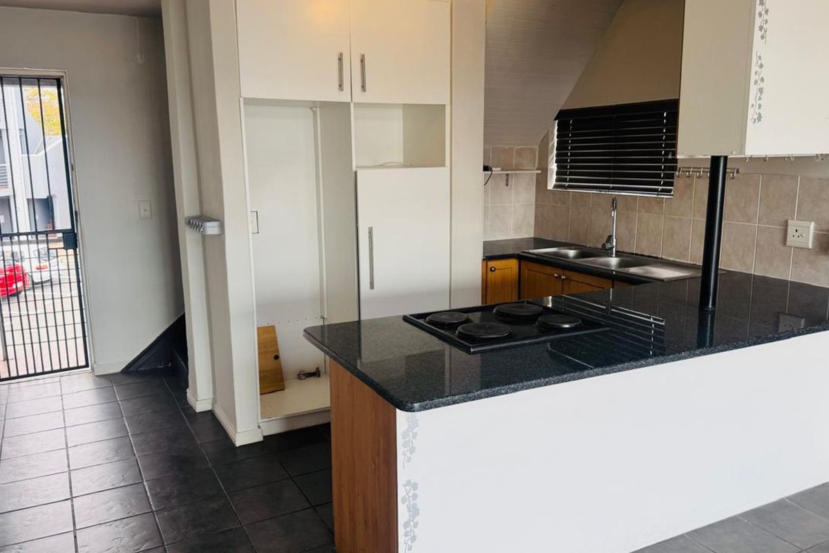 A functional kitchen featuring dark granite countertops, an electric hob, built-in cabinetry, and tiled flooring, with an adjacent security gate leading outdoors.