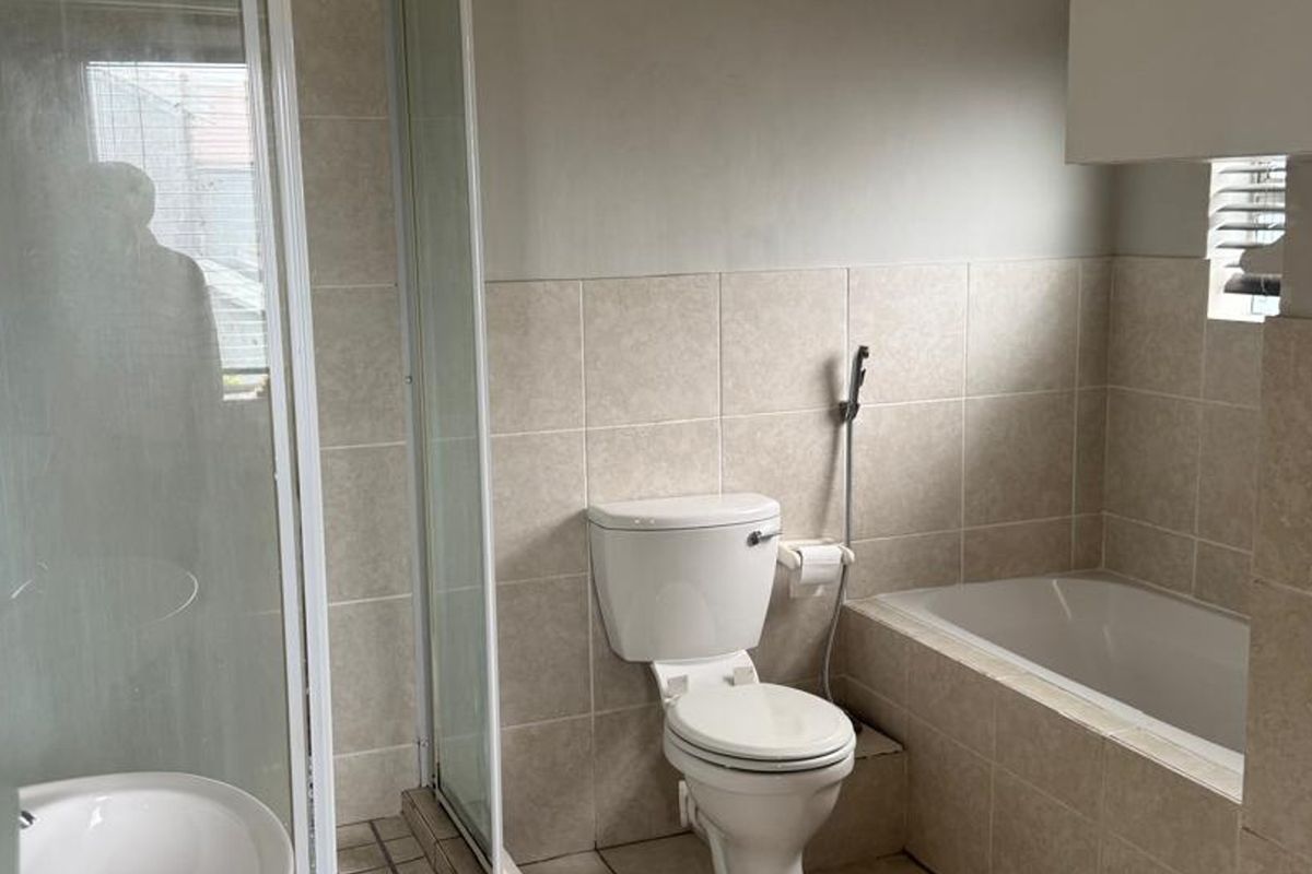 A functional bathroom featuring a separate shower enclosure, bathtub, and toilet with neutral wall tiling.