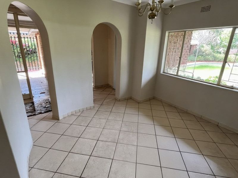An empty living area featuring tiled flooring, arched architectural doorways, and a large window providing natural light and views of the garden.