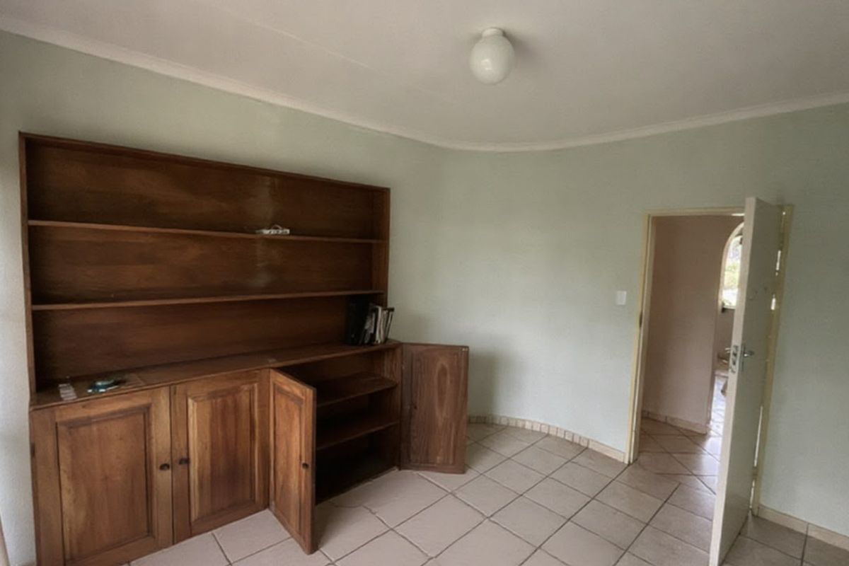 A sparsely furnished living area featuring built-in wooden cabinetry, tiled flooring, and neutral wall finishes, offering a blank canvas for renovation.