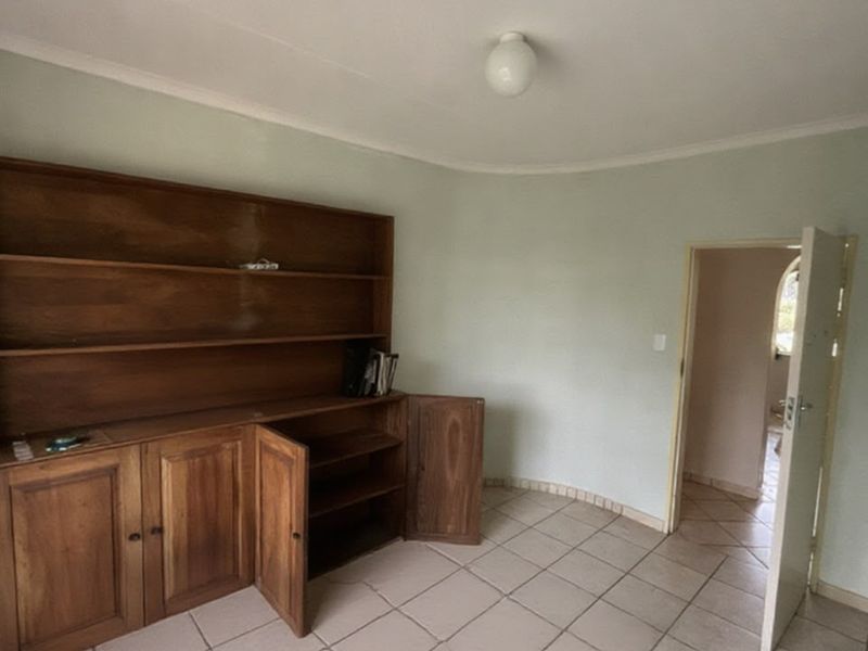 A sparsely furnished living area featuring built-in wooden cabinetry, tiled flooring, and neutral wall finishes, offering a blank canvas for renovation.