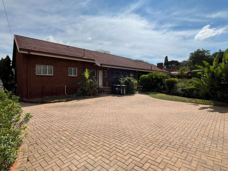 A front view of a brick house featuring a large paved driveway and established garden area.
