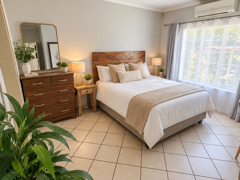 A well-maintained bedroom featuring tiled flooring, neutral wall finishes, and a wall-mounted air conditioning unit, offering a comfortable and bright living space.