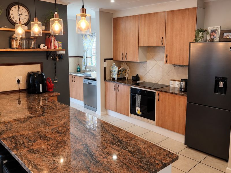 A well-maintained kitchen featuring granite countertops, wooden cabinetry, built-in oven, and a tiled backsplash, with an adjacent scullery area.
