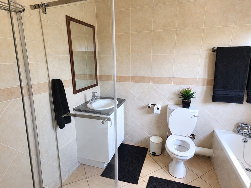 A well-maintained bathroom featuring a glass-enclosed shower, a bathtub, a vanity with a basin, and neutral wall and floor tiling.