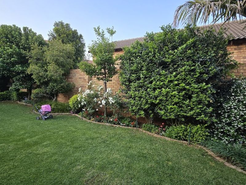 A well-maintained private garden featuring a lush lawn, mature trees, flowering shrubs, and a sturdy brick boundary wall.