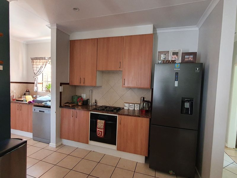 Functional kitchen featuring wood-look cabinetry, gas hob, built-in oven, tiled backsplash, and tiled flooring, with an adjacent scullery area.