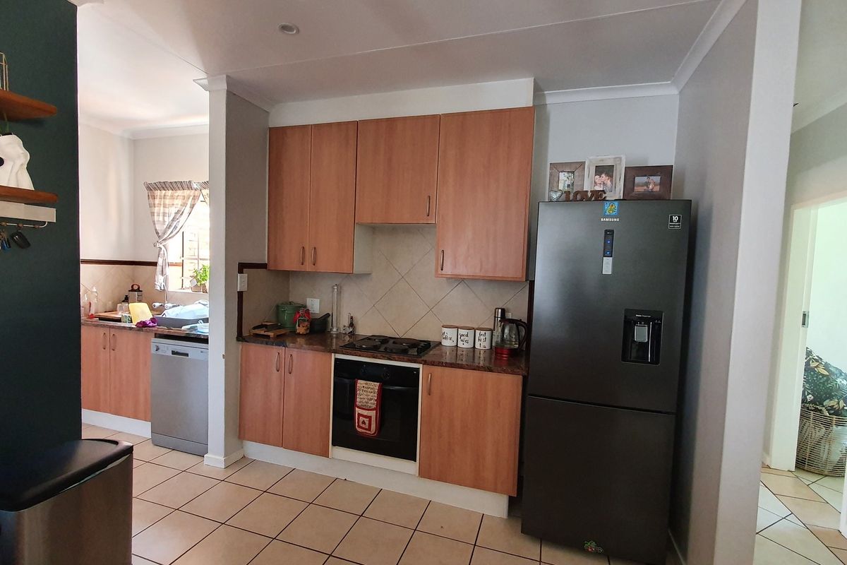 Functional kitchen featuring wood-look cabinetry, gas hob, built-in oven, tiled backsplash, and tiled flooring, with an adjacent scullery area.