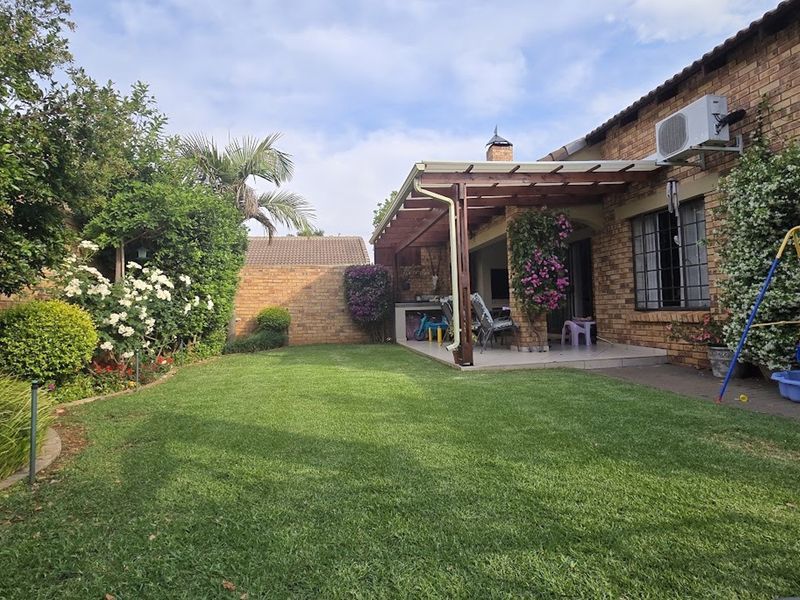 A rear garden view featuring a brick townhouse facade, a covered patio with a timber pergola, and a well-maintained lawn.