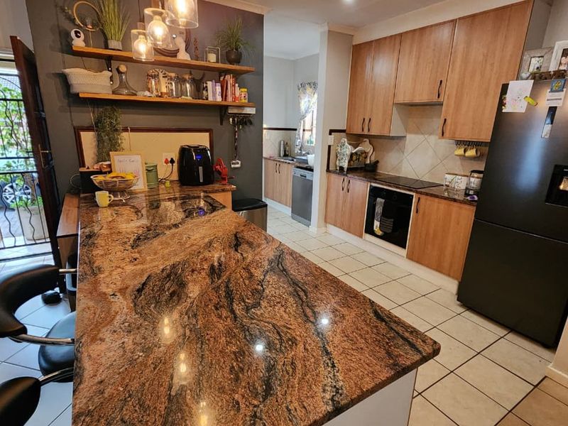 A functional kitchen featuring granite countertops, wooden cabinetry, built-in oven, and tiled flooring, with an adjacent scullery area and direct exterior access.